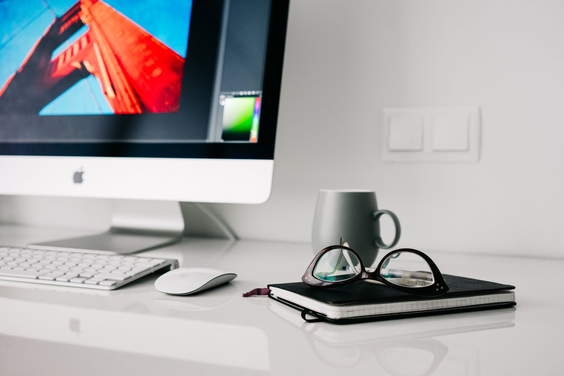 silver imac turned on beside gray ceramic mug and black frame eyeglasses
